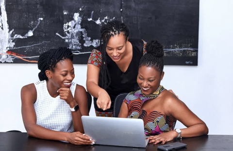 decorative photo: three smiling Black women interacting at a single laptop