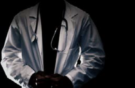 black and white photo depicting the torso of a man in a white lab coat, his hands clasped in front of him. Even in the dim light it is clear from the fingernails that the figure is Black.